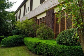 Un edificio tradicional con tejado de tejas, marcos de ventana de madera y un jardín bien cuidado con arbustos podados.