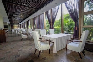 Comedor con mesas y sillas, ventanas amplias con cortinas y un techo con diseño de cuadrícula.