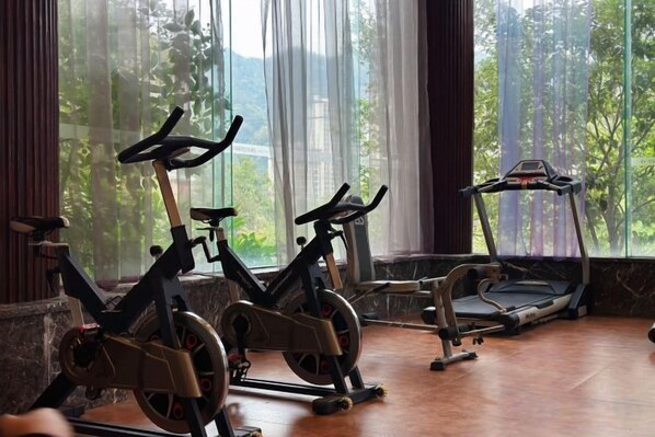 Un gimnasio con bicicletas estáticas y una caminadora, ventanas amplias con vistas a zonas verdes.