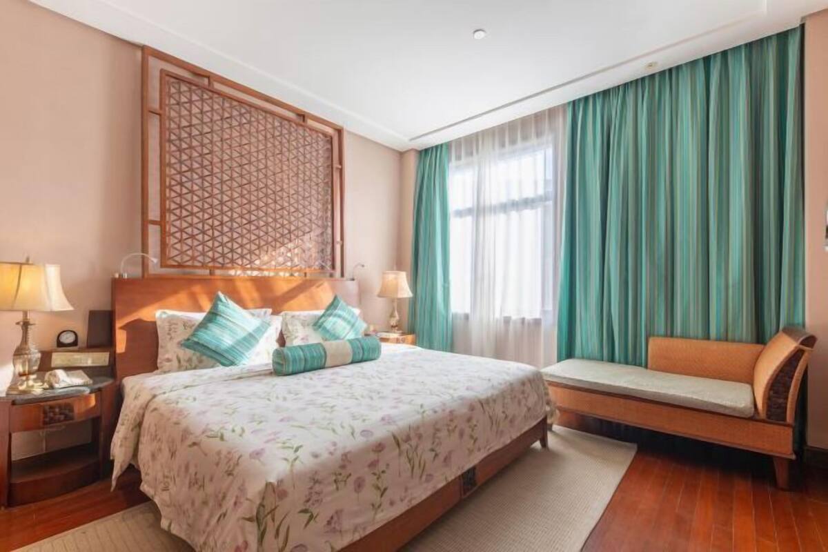 Quarto de hotel com uma cama grande, um sofá, um biombo decorativo e uma janela com cortinas.