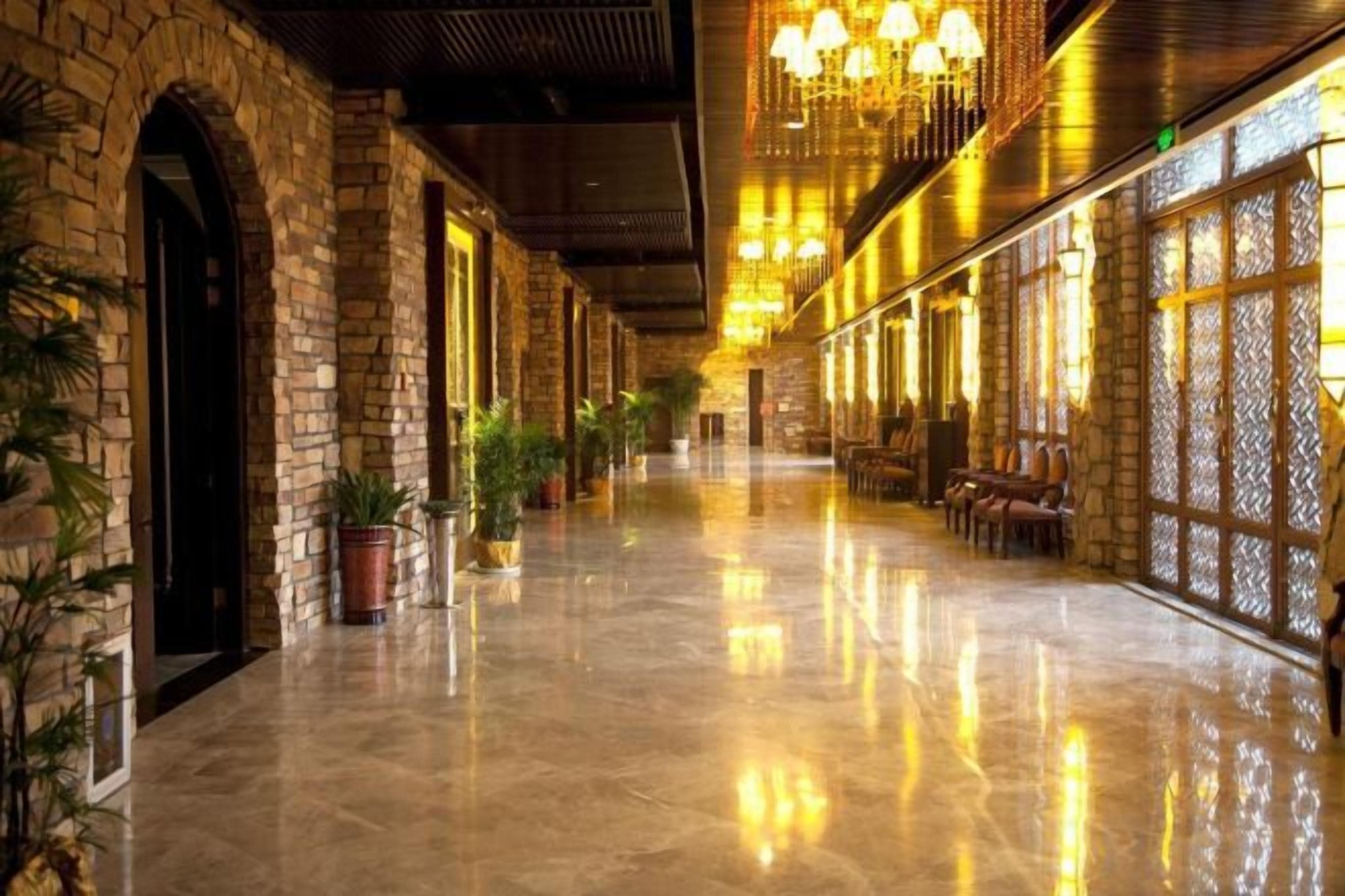 A corridor with stone walls, potted plants, and a reflective floor.