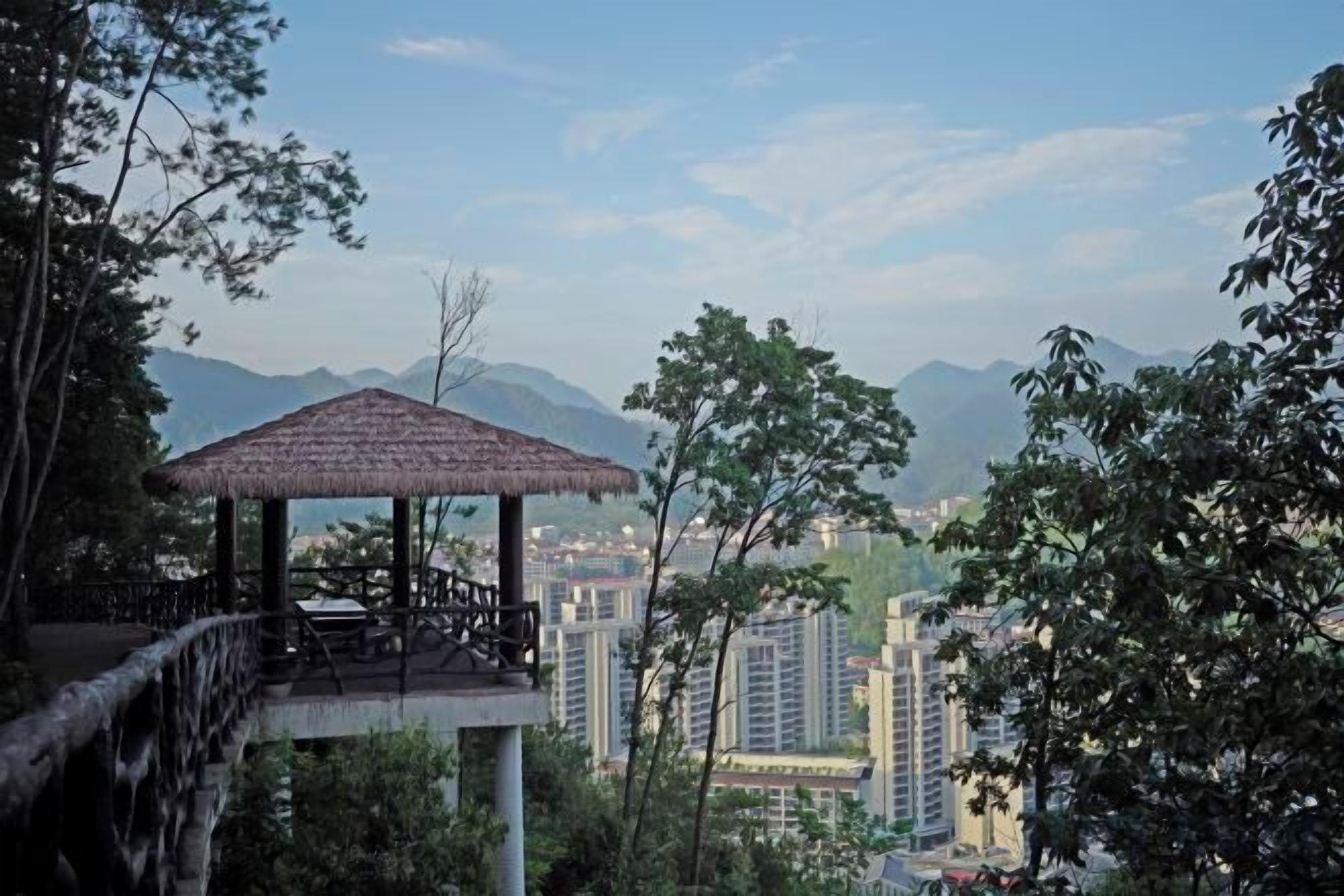 Un mirador con techo de paja que domina un paisaje urbano con montañas al fondo.