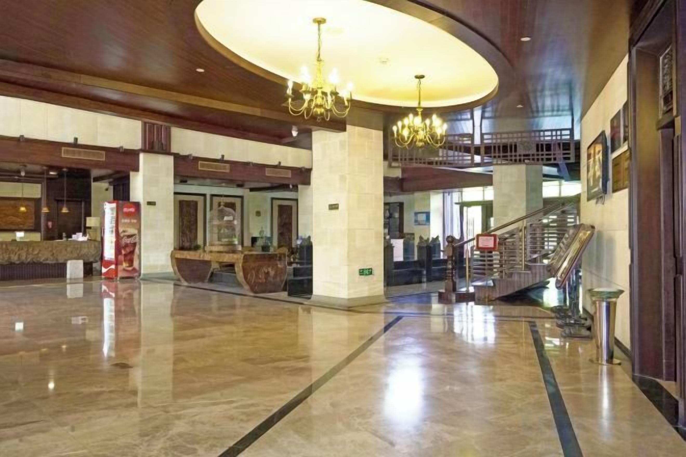 A spacious lobby with a grand chandelier, a reception desk, and a staircase leading to upper floors.