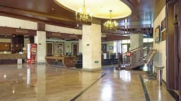 A spacious lobby with a grand chandelier, a reception desk, and a staircase leading to upper floors.
