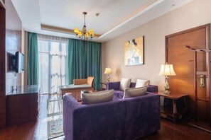Habitación de hotel con sofá morado, televisor, escritorio, lámpara y una puerta grande de madera.
