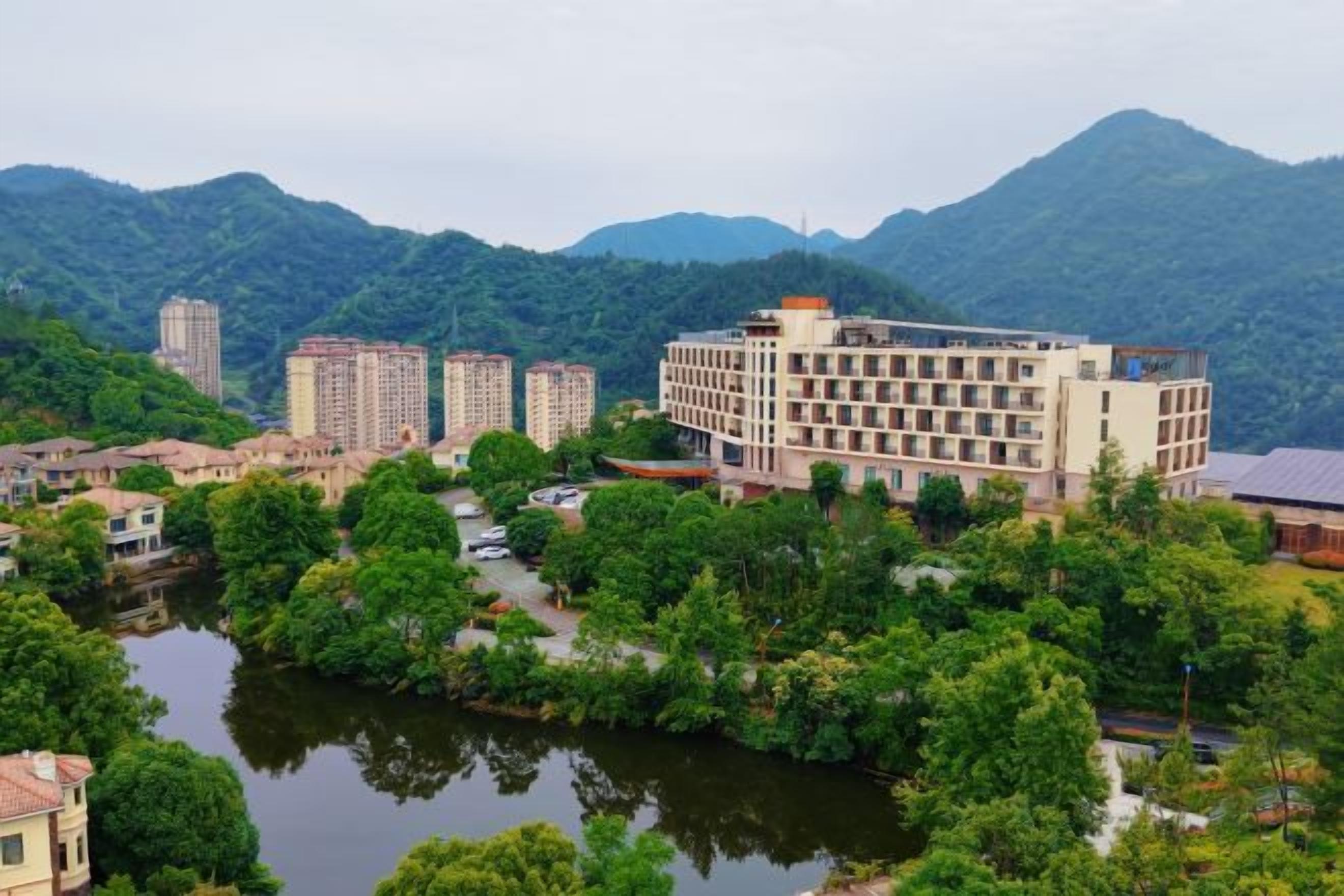 Um hotel com um rio ao primeiro plano, rodeado por vegetação e montanhas ao fundo.