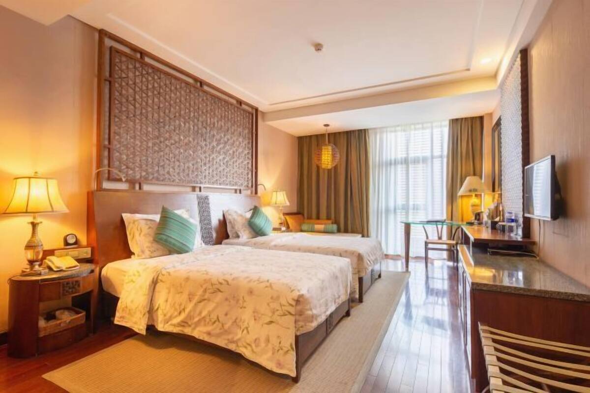 Quarto de hotel com duas camas, televisão, escrivaninha e uma janela grande.