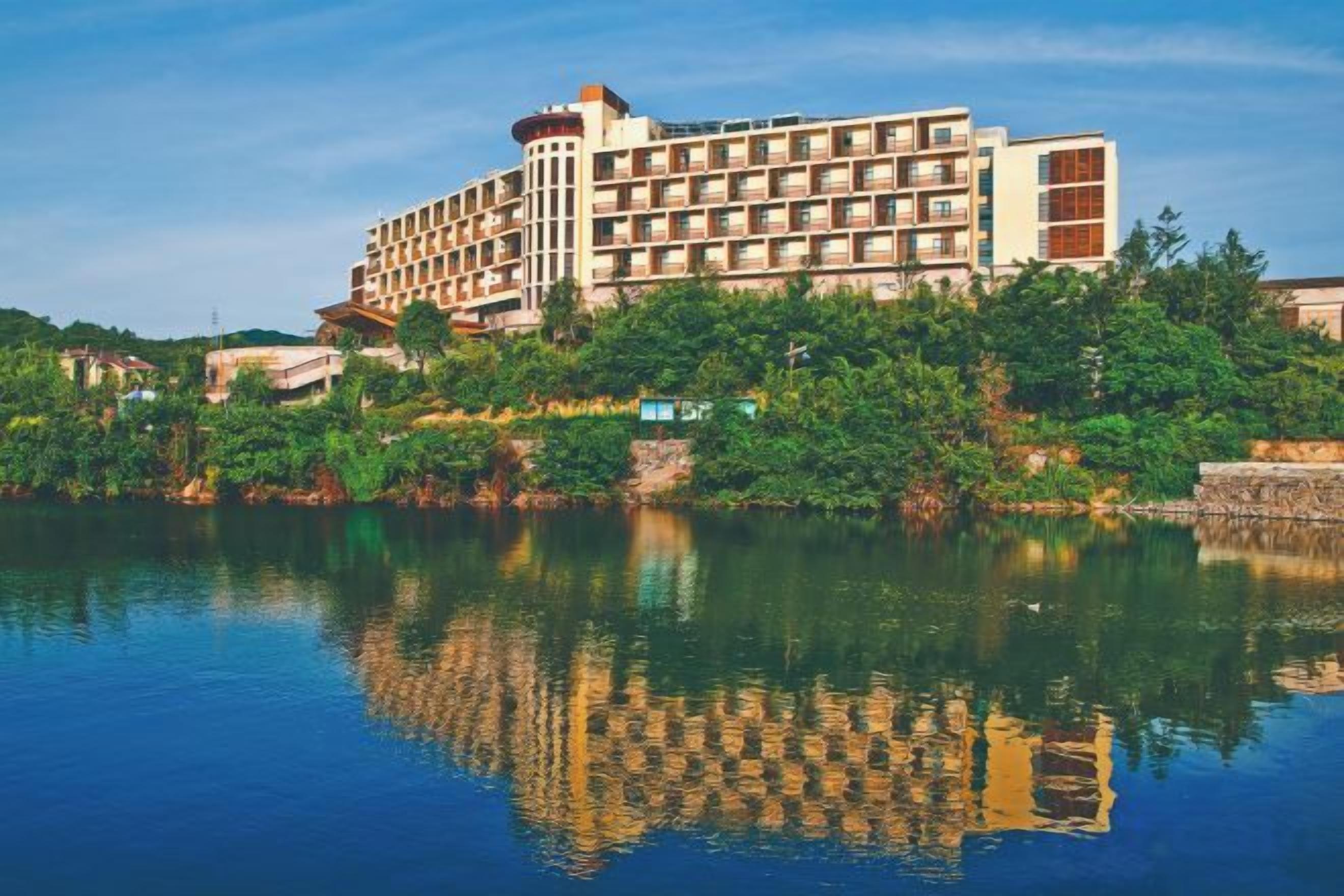 A multi-story hotel with a reflection in the water, surrounded by greenery.