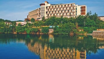 A multi-story hotel with a reflection in the water, surrounded by greenery.