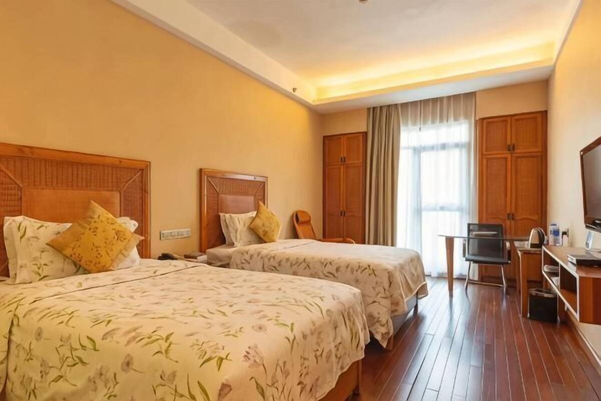 Quarto de hotel com duas camas, uma escrivaninha, uma televisão e um guarda-roupa.