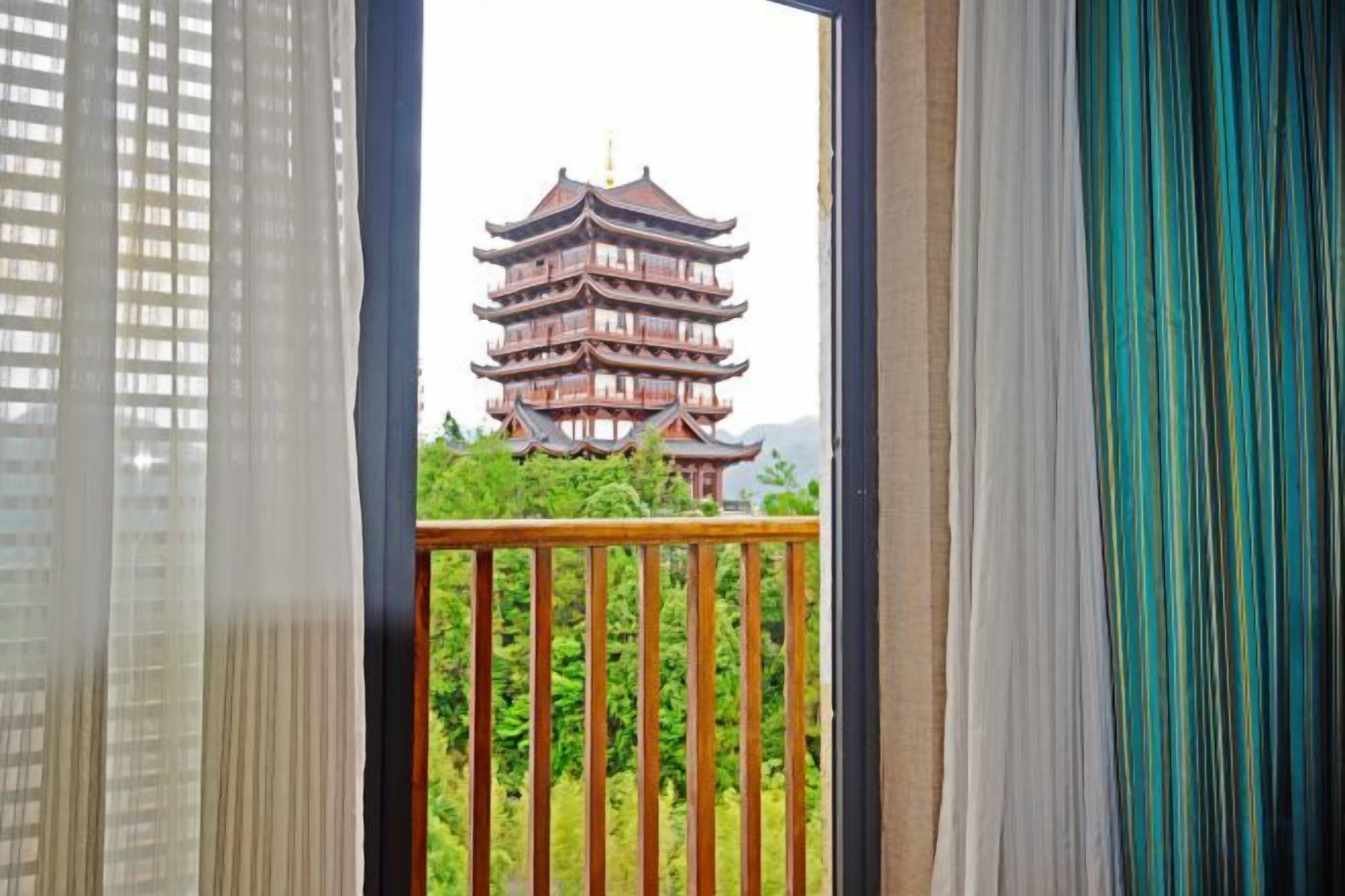 Une pagode traditionnelle à plusieurs niveaux, vue à travers un balcon orné d’une balustrade en bois.