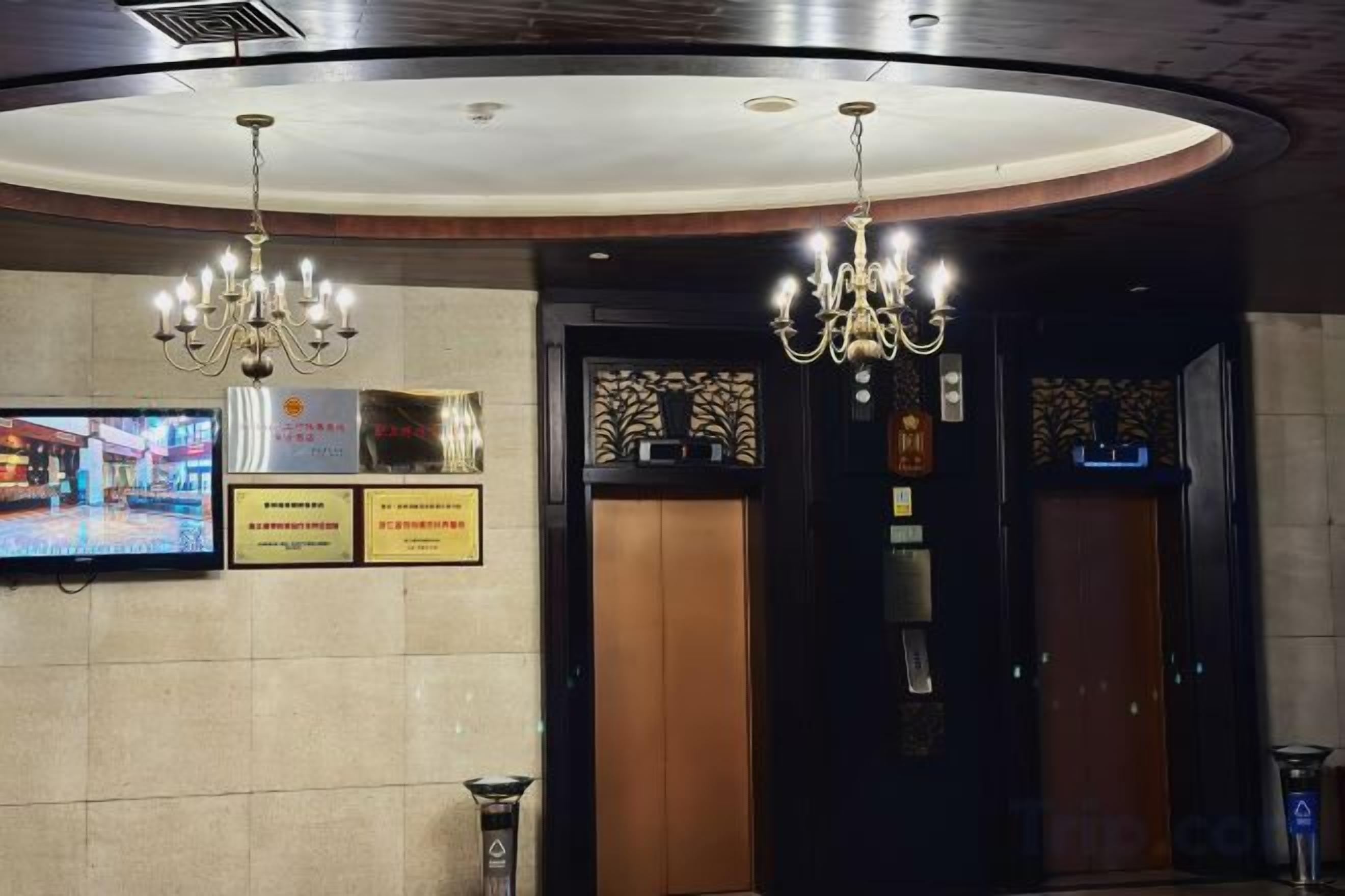 A hotel lobby with chandeliers, a television, and two elevators.
