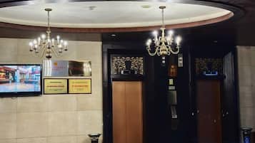 A hotel lobby with chandeliers, a television, and two elevators.