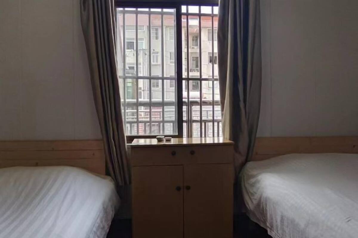 A room with two beds, a window with metal bars, and a wooden cabinet.