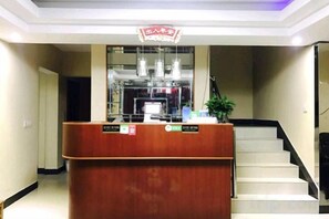 A reception desk with a sign above it, a staircase to the right, and a plant on the desk. - Xinjie Hostel (Shanghai)