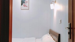 Una cama individual con ropa de cama blanca, cabecera de madera, lámpara de pared y un cuadro en la pared.