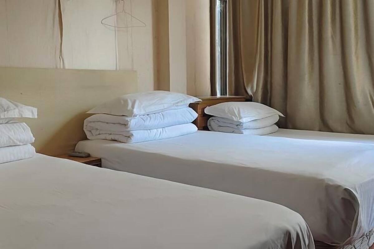 A hotel room with two beds, a wooden headboard, a window with curtains, and a hanging light fixture.