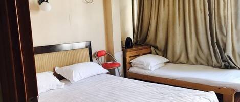 A hotel room with two single beds, a wooden headboard, a red chair, and a window with curtains.