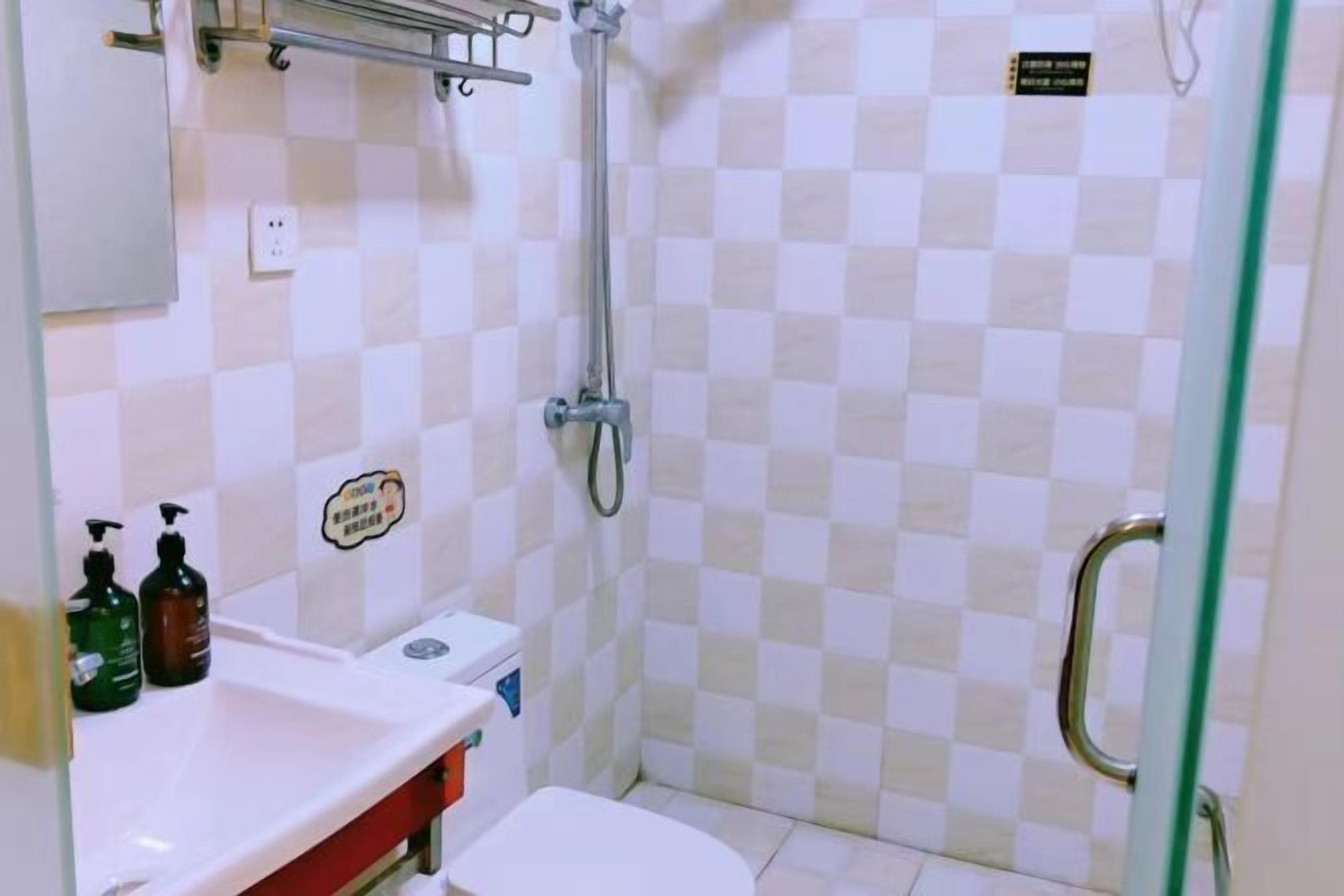 A small bathroom with a toilet, sink, and shower. There are toiletries on the sink and a sign on the wall.