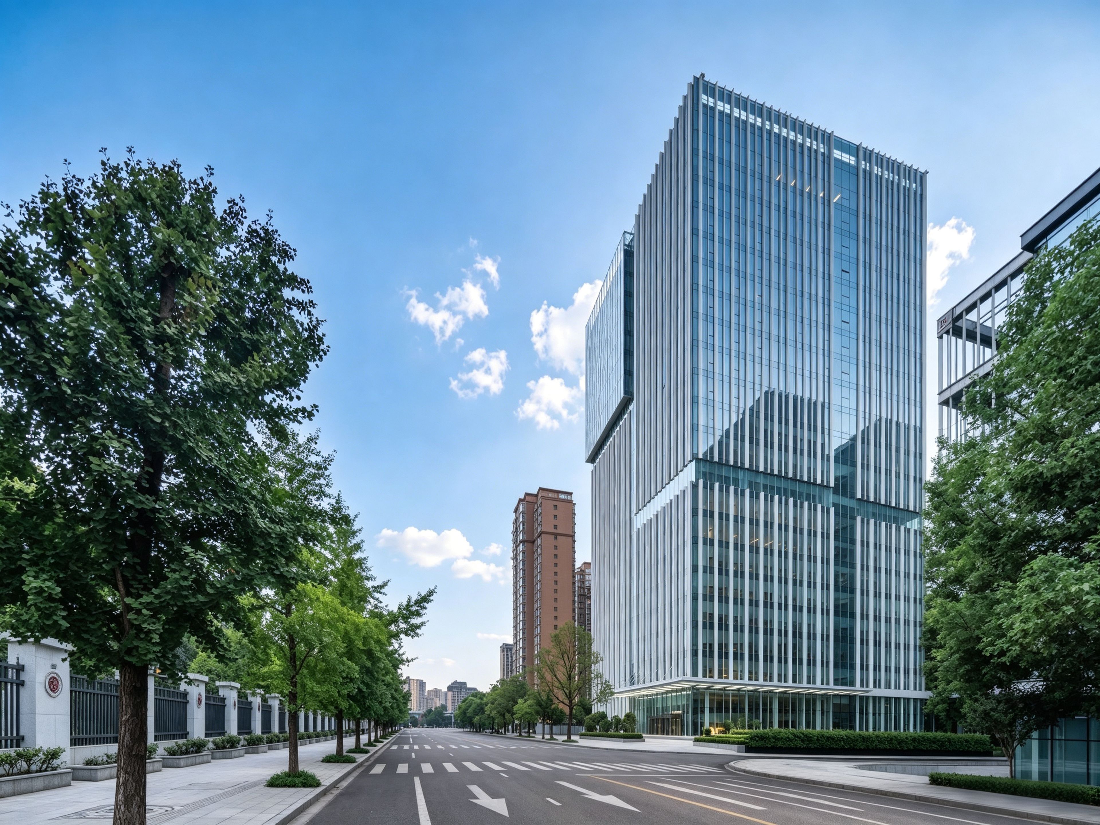A modern building with a glass facade, a wide street with trees, and a clear sky.