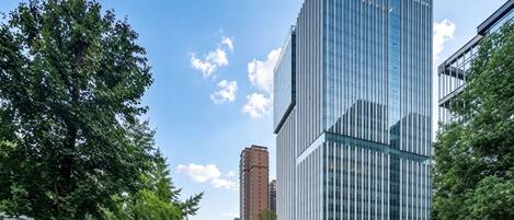 A modern building with a glass facade, a wide street with trees, and a clear sky.