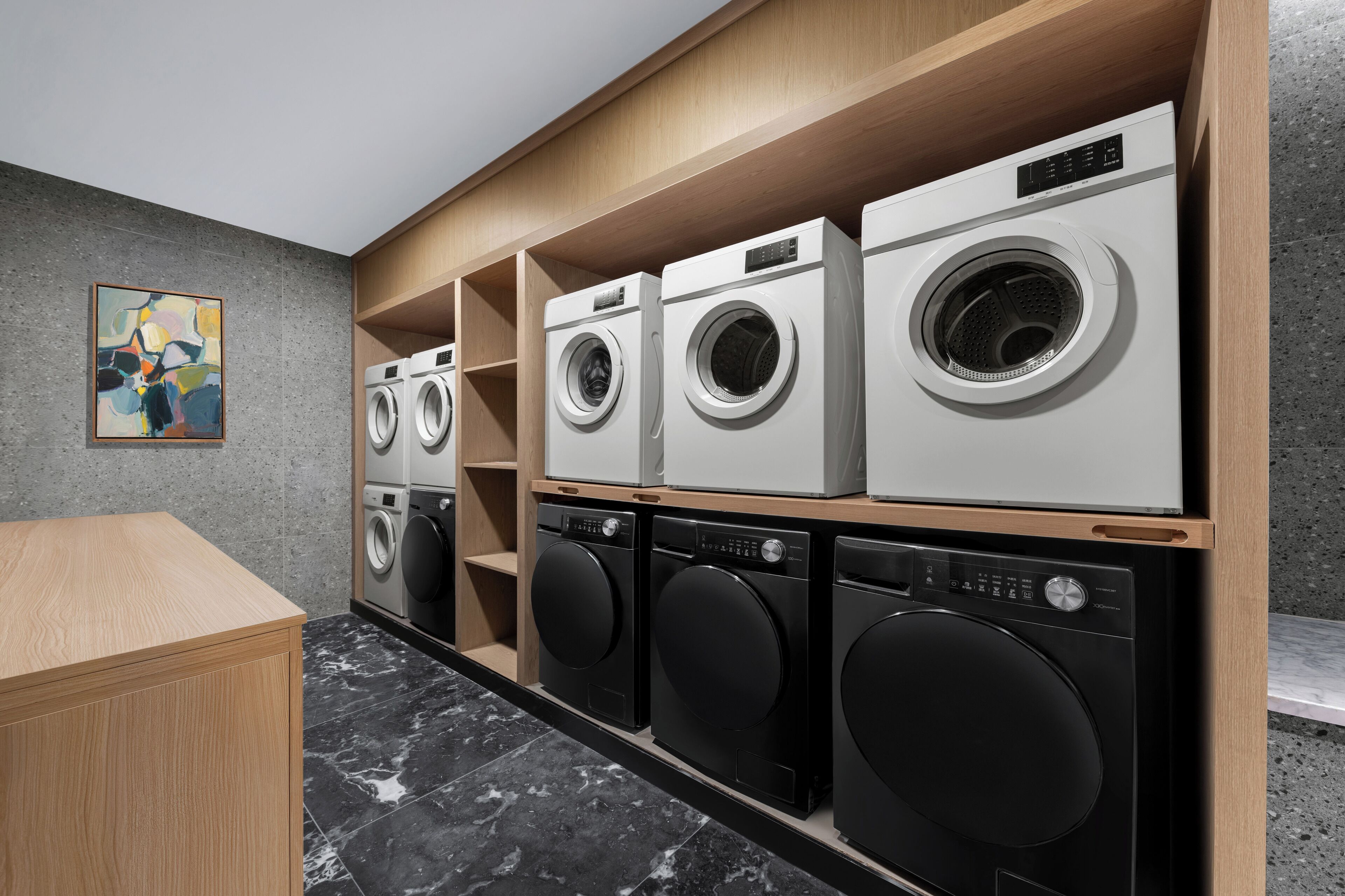 A laundry room with multiple washing machines and dryers, wooden shelving, and a marble floor.