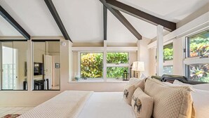 Un dormitorio con una cama grande, varias ventanas y vistas a zonas verdes.