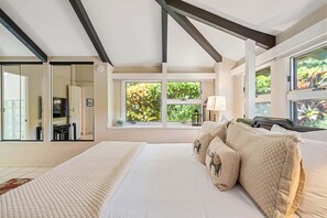 Ein Schlafzimmer mit einem großen Bett, mehreren Fenstern und Blick auf Grün.