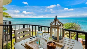 Een balkon met een tafel gedekt voor twee, met uitzicht op een strand met helderblauw water en een berg in de verte.