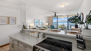 Een moderne keuken met een groot eiland, uitzicht op de oceaan en een balkon met zitplaatsen buiten.