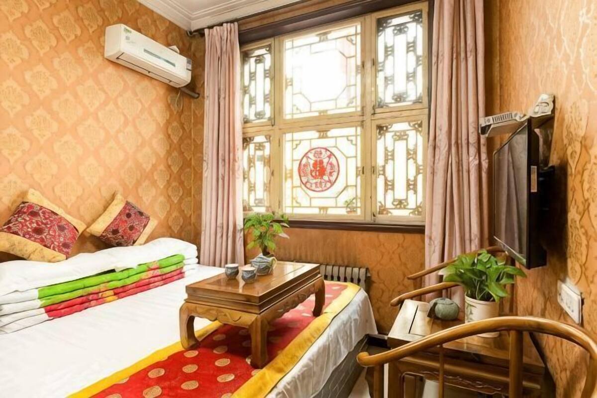 Une chambre d’hôtel avec un lit, une table en bois, une chaise, une fenêtre avec des rideaux et un radiateur.
