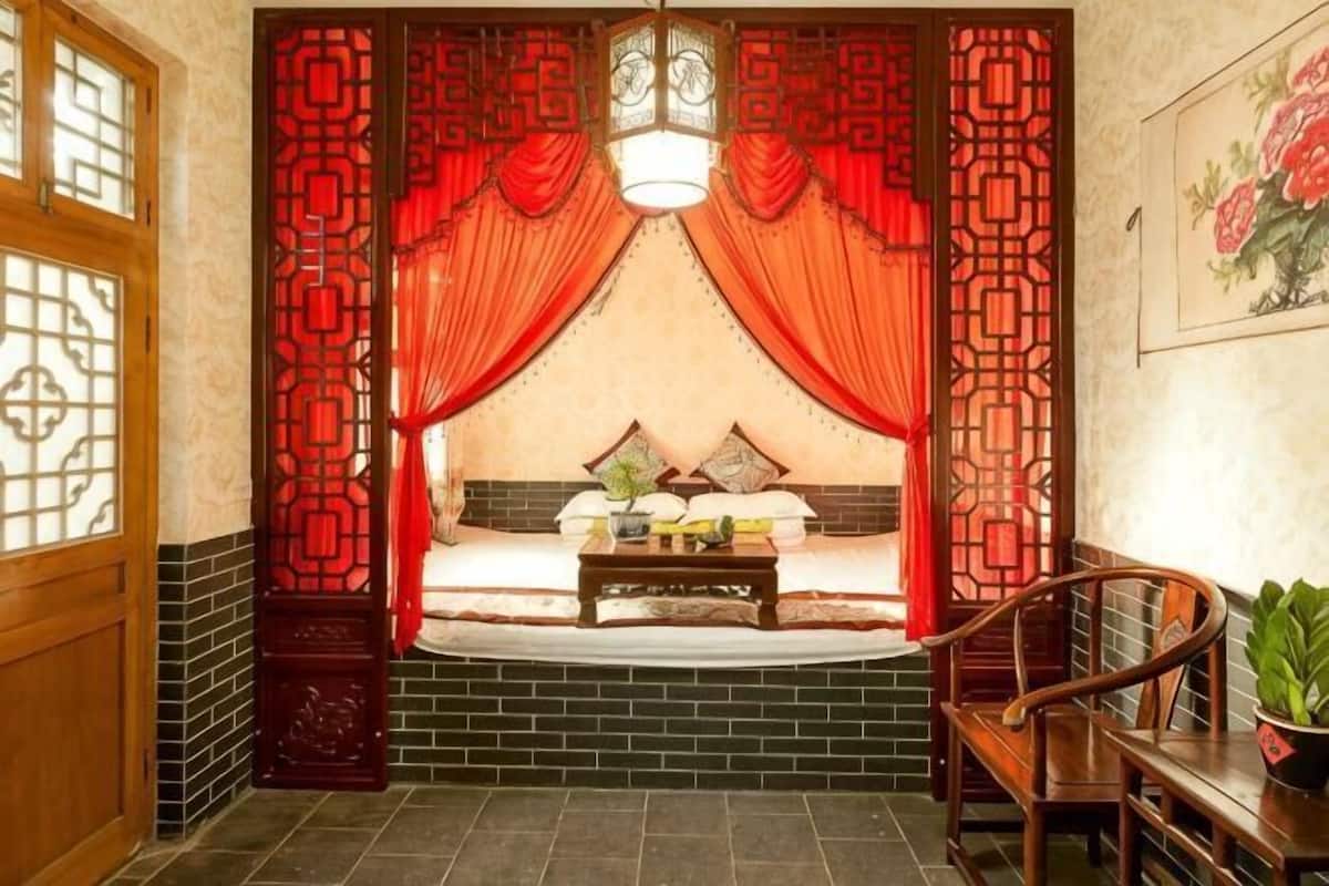 Une chambre traditionnelle avec un lit, des rideaux, une chaise en bois et une table.