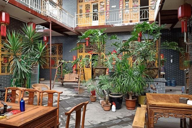 Un patio con una mesa y sillas de madera, plantas en macetas y un edificio tradicional con balcón.