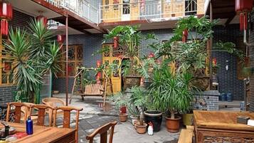 Un patio con una mesa y sillas de madera, plantas en macetas y un edificio tradicional con balcón.