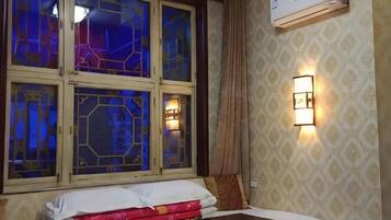 Habitación de hotel con cama, mesita de noche, ventana con vitral y aire acondicionado de pared.