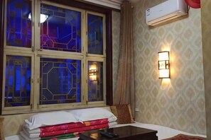 A hotel room with a bed, a nightstand, a window with stained glass, and a wall-mounted air conditioner. - Pingyao Jiaxin Guesthouse (Pingyao County)