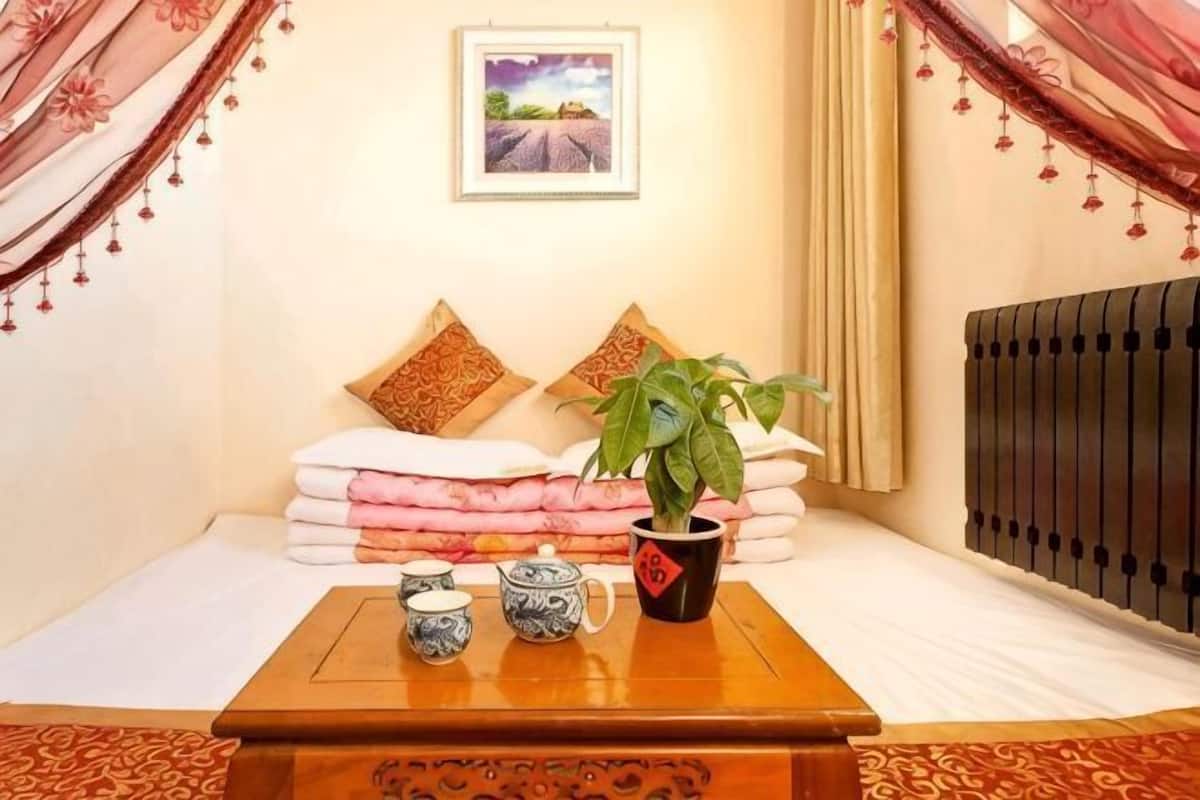 Une chambre à coucher bien rangée, avec un lit, des oreillers, une table de chevet agrémentée d’une plante et de tasses à thé, et un tableau encadré accroché au mur.