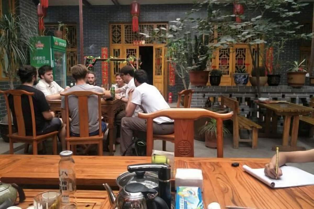 A group of people seated around a wooden table in a restaurant with traditional decor, including potted plants and red lanterns.