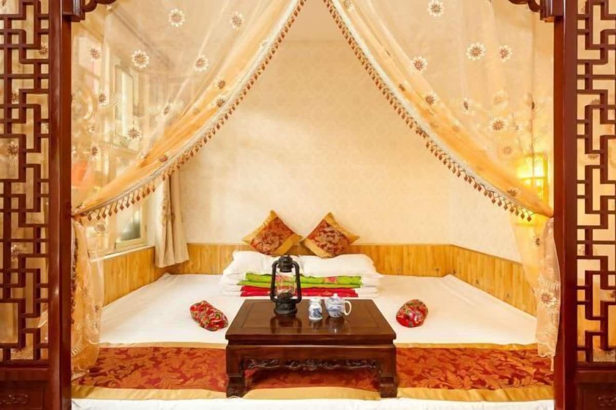Un lit traditionnel avec un baldaquin, des oreillers, une table de chevet avec une lanterne et un mur décoratif.