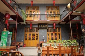 A traditional Chinese courtyard with a wooden table and chairs, a balcony, and red lanterns. - Pingyao Jiaxin Guesthouse (Pingyao County)