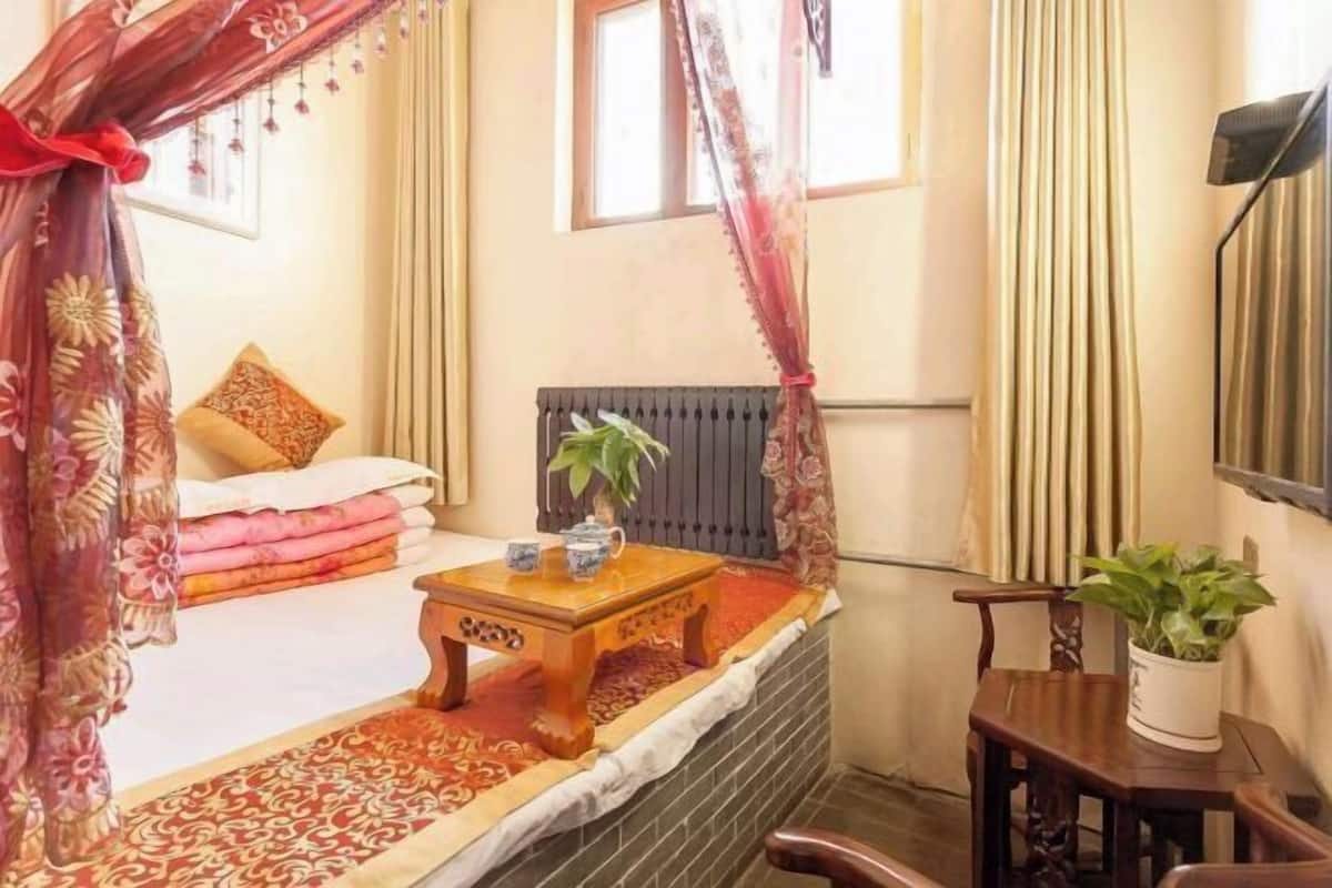 Une chambre à coucher avec un lit, une table de chevet ornée d’une plante, un radiateur et une fenêtre avec des rideaux.