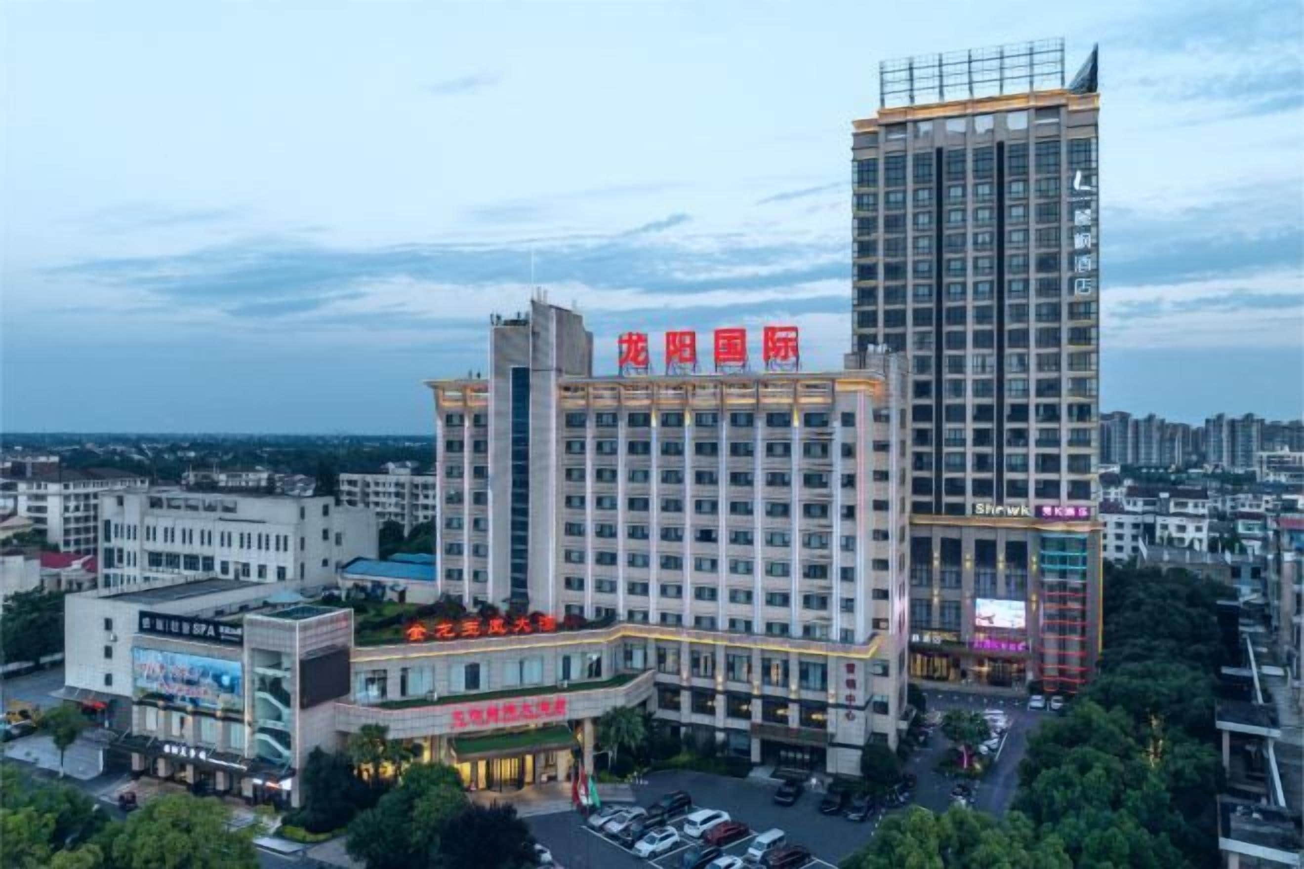 A multi-story hotel with a prominent sign at the top, surrounded by other buildings and a parking area.