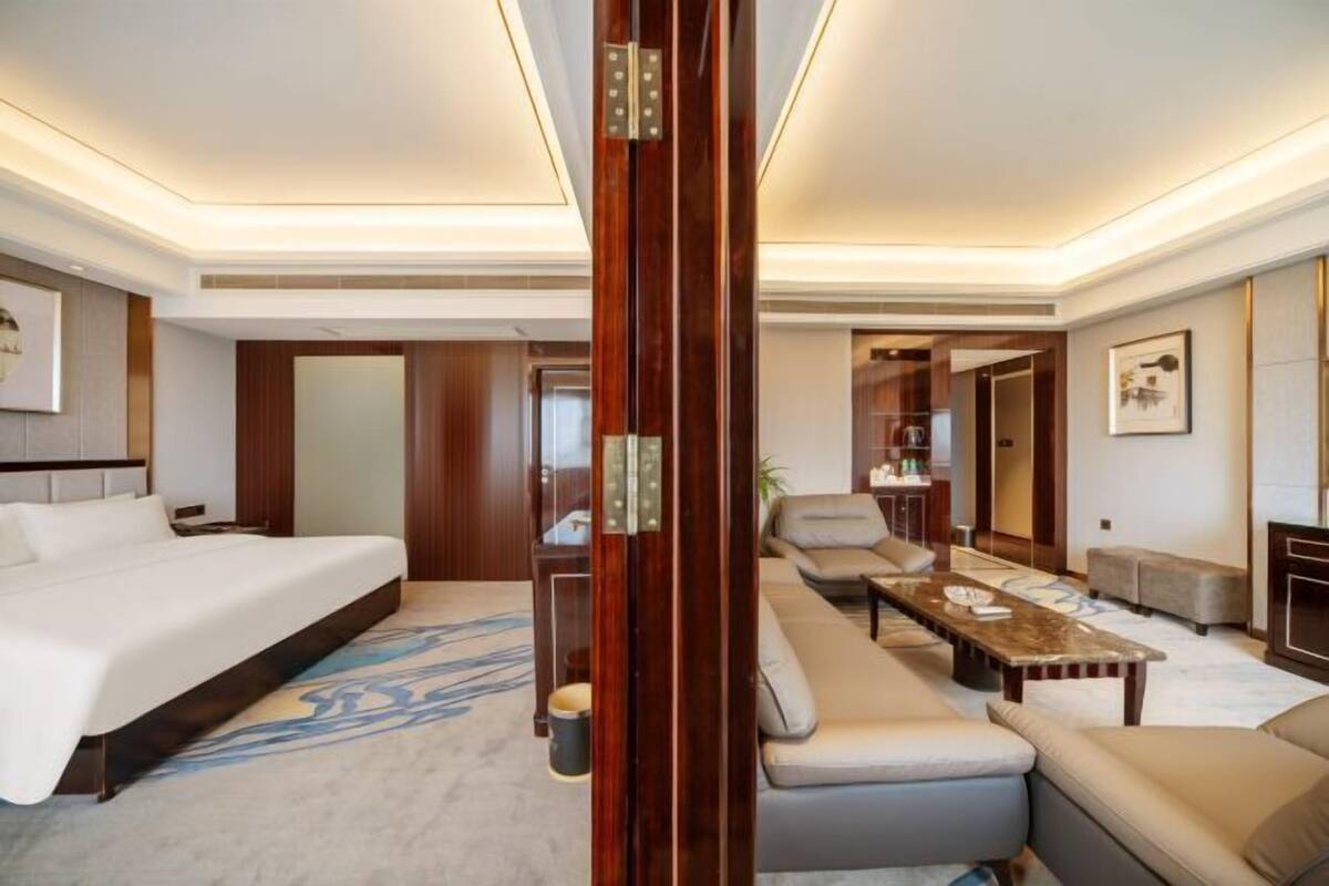 A hotel room with a bed, sofa, coffee table, and a wooden partition.