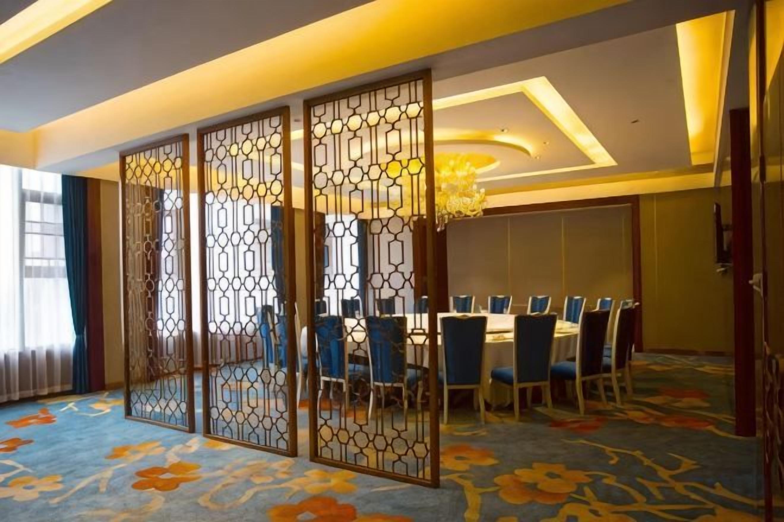 A hotel room with a dining area, a decorative screen, and a chandelier.