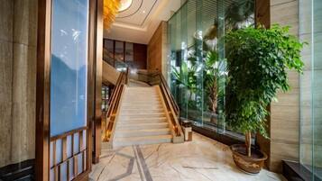 A hotel lobby with a marble floor, a staircase, and a potted plant.