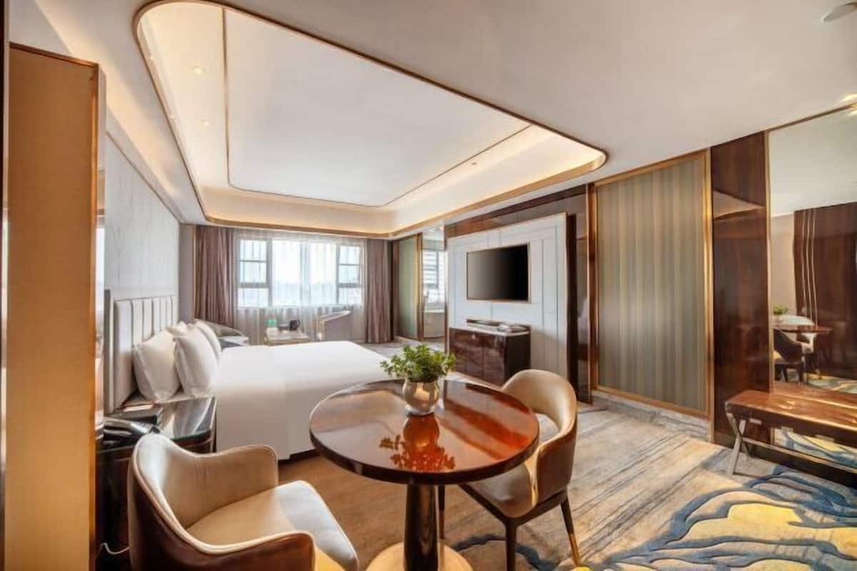 A hotel room with a bed, a desk, a TV, and a dining area with chairs and a table.