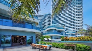 A modern hotel with a curved facade, outdoor seating area, and lush greenery.
