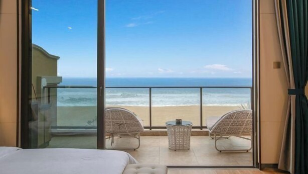 A balcony with a view of the ocean, two wicker chairs, a small table, and a bed.
