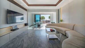 A modern living room with a flat-screen TV, a sofa, a coffee table, and a dining area with a view.
