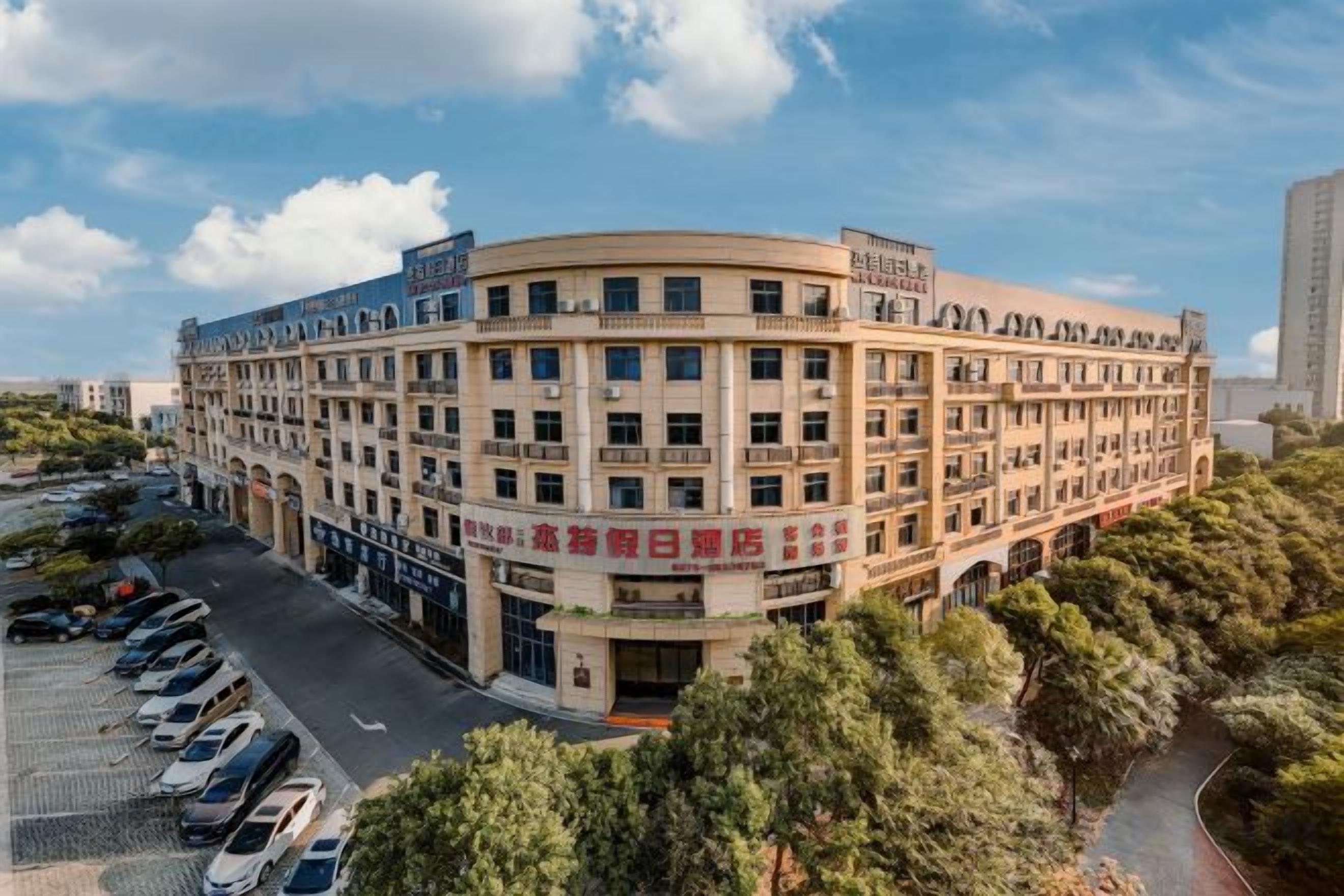 A multi-story hotel with a curved facade, a parking lot, and a landscaped area with trees.
